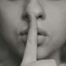 vrouw doet haar vinger tegen haar lippen als teken voor een geheim