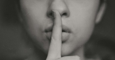 vrouw doet haar vinger tegen haar lippen als teken voor een geheim