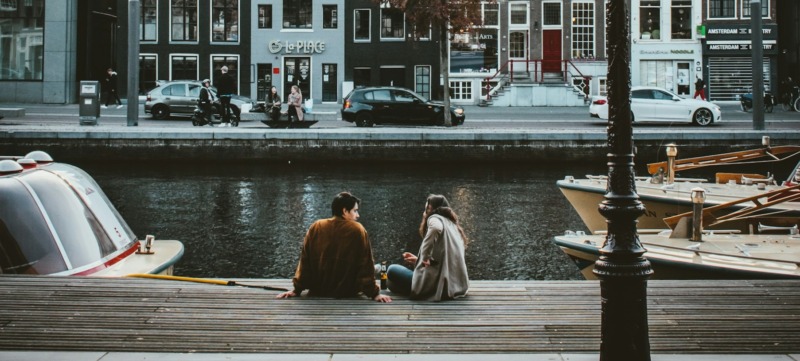 twee mensen praten met elkaar aan de gracht in amsterdam en besteden hun vrije tijd samen