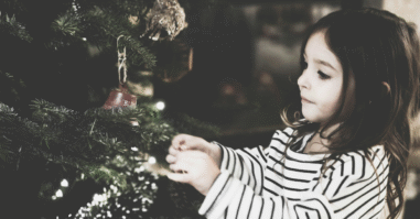Een meisje die bij de kerstboom staat