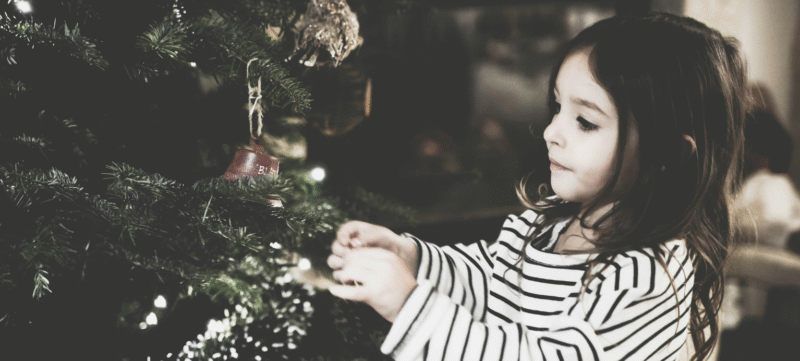Een meisje die bij de kerstboom staat