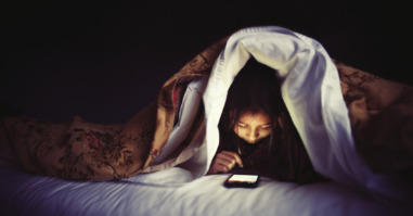 kind zit op haar smartphone in bed