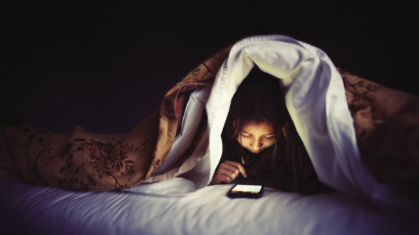 kind zit op haar smartphone in bed