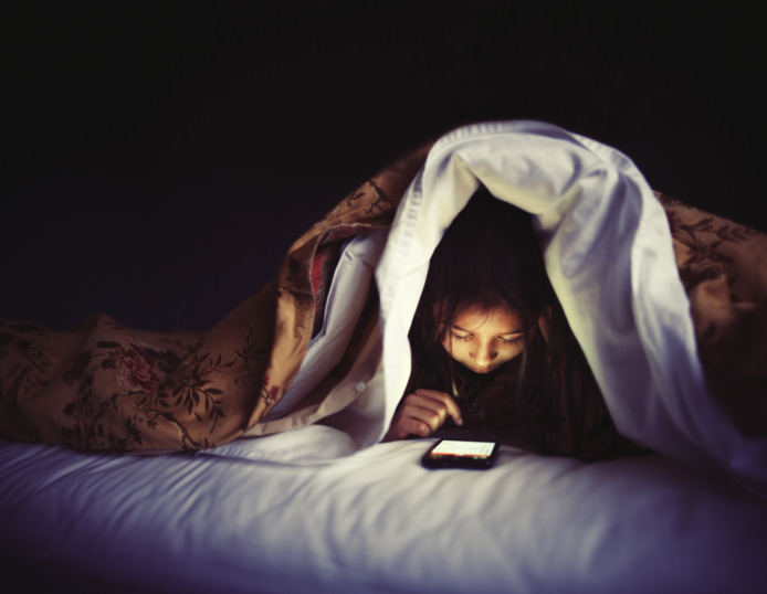 kind zit op haar smartphone in bed
