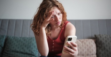 foto van een vrouw die fronsend naar haar telefoon kijkt ter illustratie bij een artikel over hypernormalisatie
