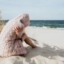 Vrouw die verdrietig op het strand zit als beeld bij tekst over zomerdepressie