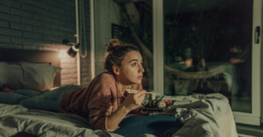 Vrouw die sushi eet en een serie aan het bingewatchen is in bed.