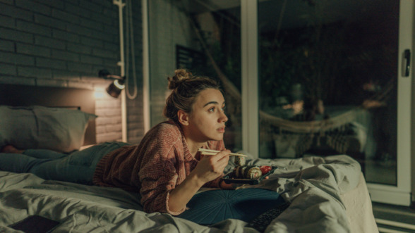 Vrouw die sushi eet en een serie aan het bingewatchen is in bed.