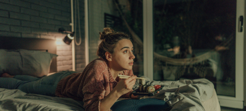 Vrouw die sushi eet en een serie aan het bingewatchen is in bed.