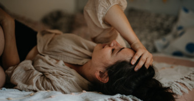 Vrouw ligt op bed door menstruatiepijn en voelt zich eenzaam.