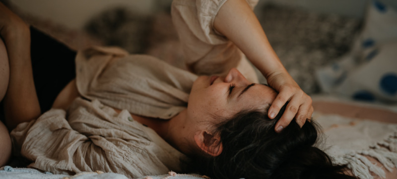 Vrouw ligt op bed door menstruatiepijn en voelt zich eenzaam.