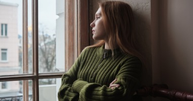 vrouw kijkt angstig uit het raam