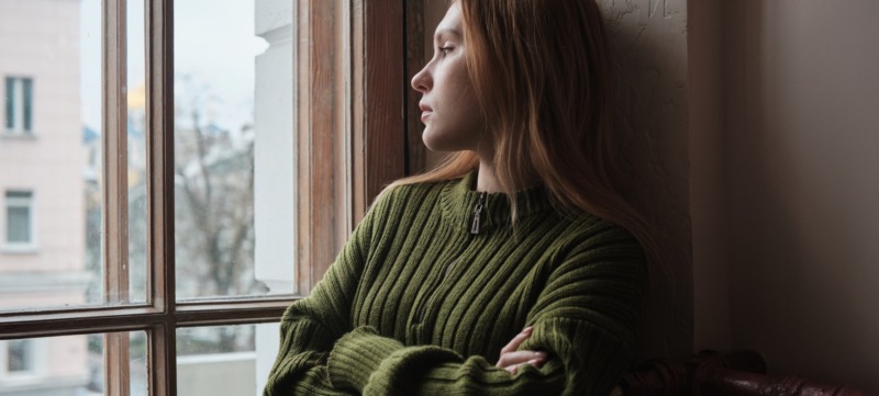 vrouw kijkt angstig uit het raam