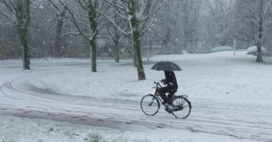 A woman ride bicycle and take cover with umbrella during snowfall at the Rembrandt park in Amsterdam,Netherlands.