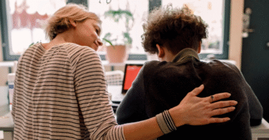 Vrouw legt een hand op de rug van een jongen om hem gerust te stellen.