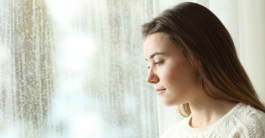 Vrouw kijkt uit het raam met een leegte in haar blik