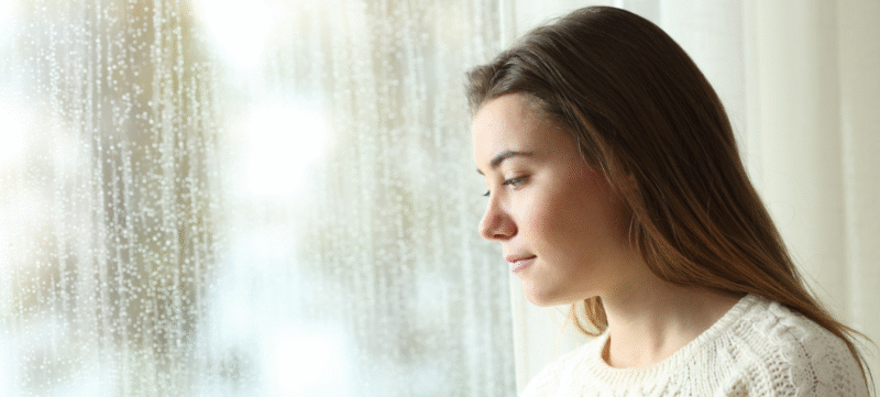Vrouw kijkt uit het raam met een leegte in haar blik
