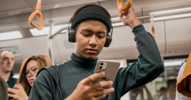 persoon staat in de metro na een drukke dag op haar telefoon te kijken en schermt zich af voor prikkels met een koptelefoon
