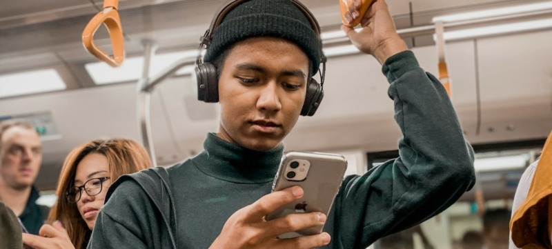 persoon staat in de metro na een drukke dag op haar telefoon te kijken en schermt zich af voor prikkels met een koptelefoon