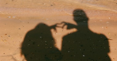 schaduw van twee mensen in een relatie die een hartje maken met hun handen
