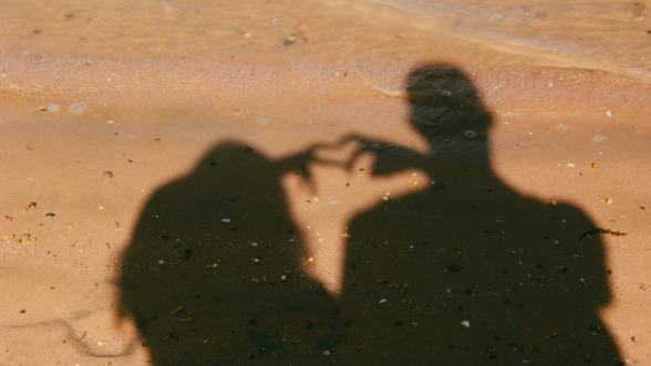 schaduw van twee mensen in een relatie die een hartje maken met hun handen