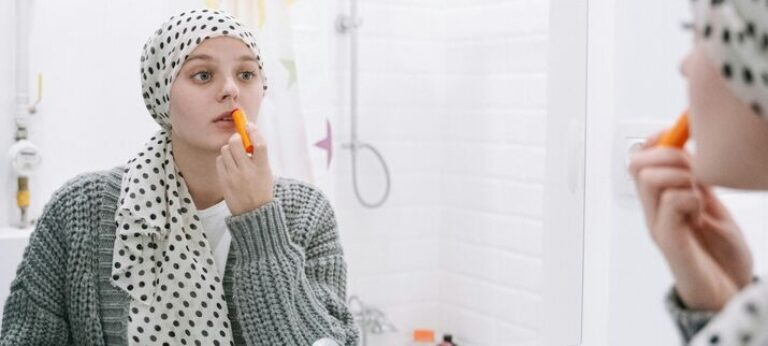 vrouw met doek om haar hoofd kijkt in de spiegel en doet lippenstift op