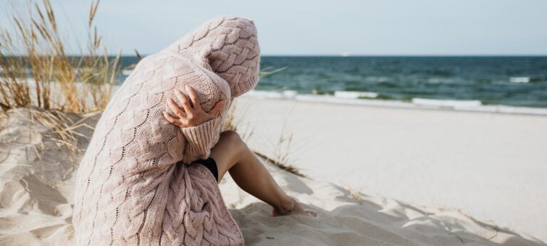 Vrouw die verdrietig op het strand zit als beeld bij tekst over zomerdepressie